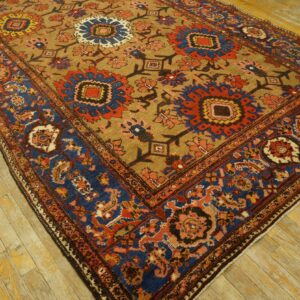 Tan field rug with bold red and blue medallions and a complex blue border, placed on worn wood flooring.
