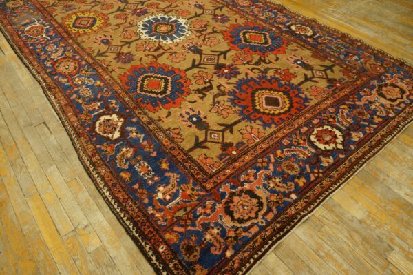 Tan field rug with bold red and blue medallions and a complex blue border, placed on worn wood flooring.