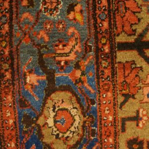 Rustic rug detail showing rust red, blue, and brown geometric patterns on light wood flooring.