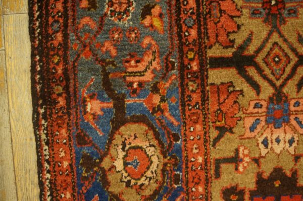 Rustic rug detail showing rust red, blue, and brown geometric patterns on light wood flooring.