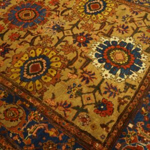 Traditional floral medallion rug in gold, navy, and red rests partially on light wood flooring.