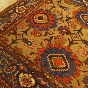 Traditional rug with complex red, blue, and tan stylized floral patterns rests on light wood planks.