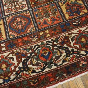 Detail of a low-pile rug showing colorful geometric compartments and an elaborate floral border on wood floor.