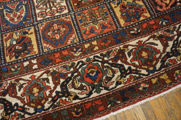 Detail of a low-pile rug showing colorful geometric compartments and an elaborate floral border on wood floor.