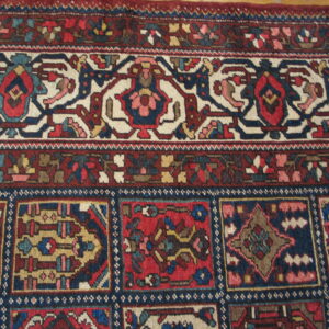 Ornate traditional rug border in red, navy blue, and cream above a dense field of geometric squares.