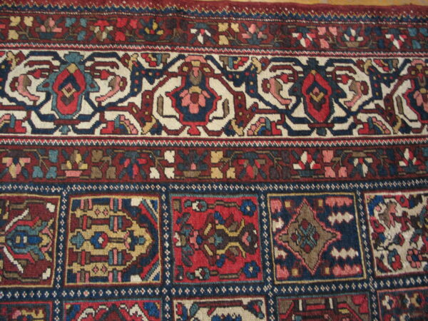 Ornate traditional rug border in red, navy blue, and cream above a dense field of geometric squares.