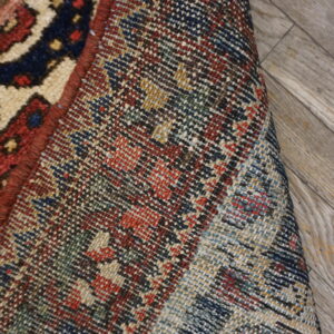 The tight, multicolored woven backing is visible next to the patterned pile of the partially rolled rug.
