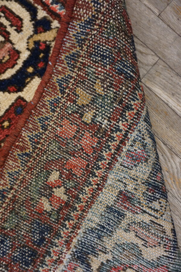 The tight, multicolored woven backing is visible next to the patterned pile of the partially rolled rug.
