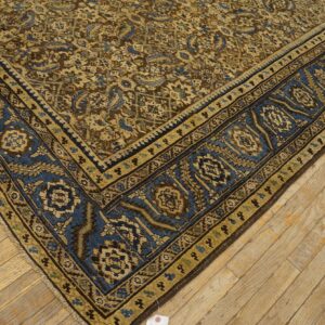 Tan, blue, and brown patterned rug corner resting on light, distressed wooden floorboards.