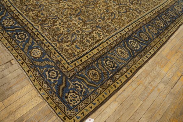 Tan, blue, and brown patterned rug corner resting on light, distressed wooden floorboards.
