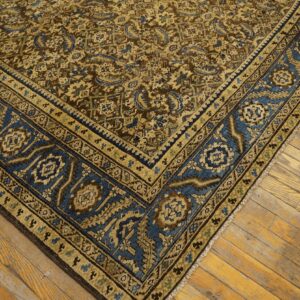 Brown and gold patterned rug with a wide blue geometric border resting on light wood flooring.