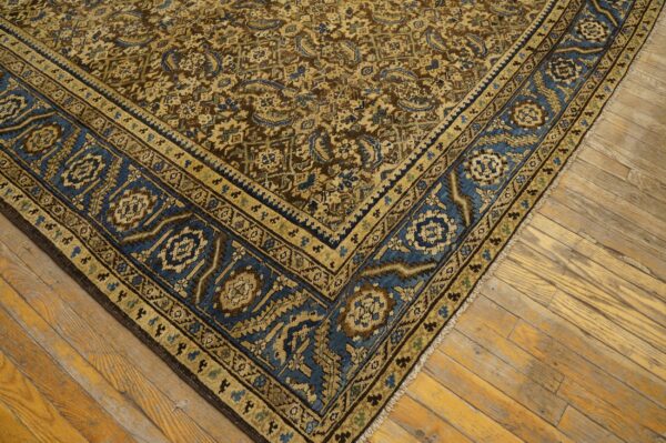 Brown and gold patterned rug with a wide blue geometric border resting on light wood flooring.