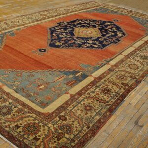 Orange and navy medallion rug with detailed tan and blue borders on rustic, light wooden flooring.