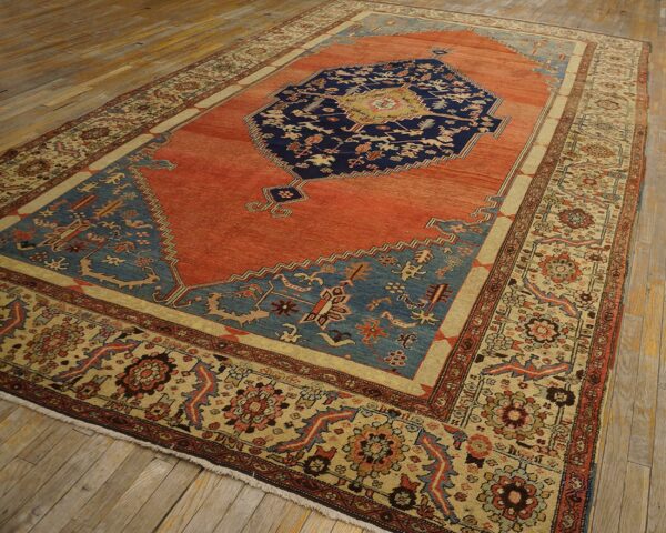 Ornate rug with a rust field, navy central medallion, and elaborate cream borders set on light wood flooring.