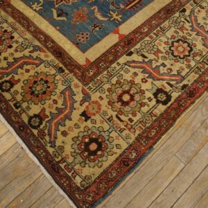 Corner detail of a low-pile rug with blue, red, and beige floral patterns on rustic wood planks.