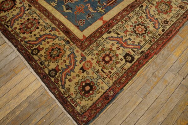 Corner detail of a low-pile rug with blue, red, and beige floral patterns on rustic wood planks.