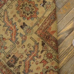 Low-pile tan rug with detailed red and blue geometric patterns rests on distressed diagonal flooring.