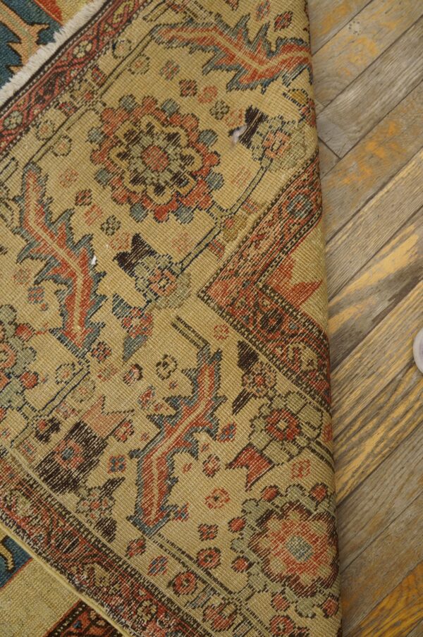 Low-pile tan rug with detailed red and blue geometric patterns rests on distressed diagonal flooring.