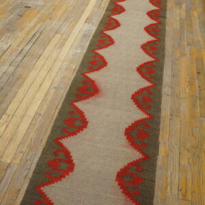 Taupe and olive flatweave runner with a red wavy pattern displayed on distressed wood planks.