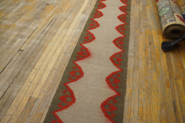 Taupe and olive flatweave runner with a red wavy pattern displayed on distressed wood planks.