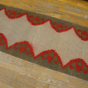 Gray and olive flatweave rug with a red zig-zag geometric pattern lies on worn hardwood planks.