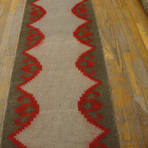 A beige and olive runner features a vibrant red serrated geometric border on worn wood planks.