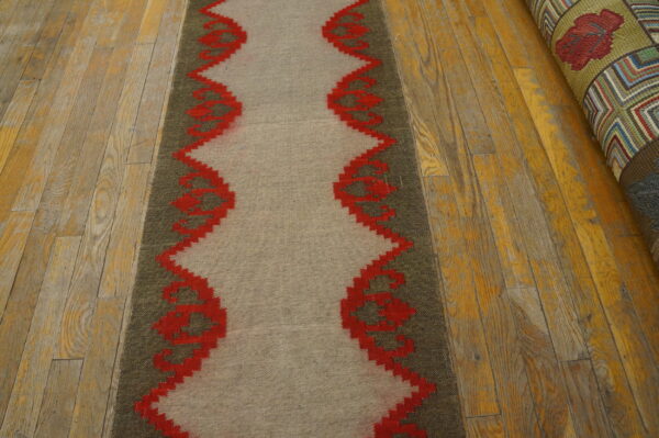 A beige and olive runner features a vibrant red serrated geometric border on worn wood planks.