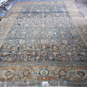 Distressed blue and tan ornate area rug with uneven pile laid on a gray concrete floor.