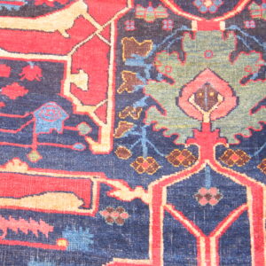 Intricate low-pile rug design featuring stylized floral motifs in red, navy, green, and tan.