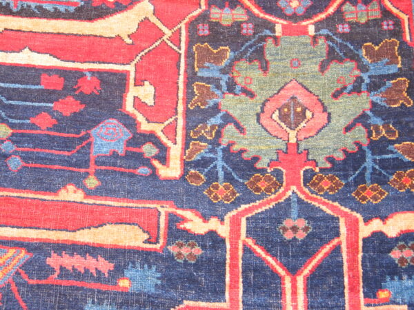 Intricate low-pile rug design featuring stylized floral motifs in red, navy, green, and tan.