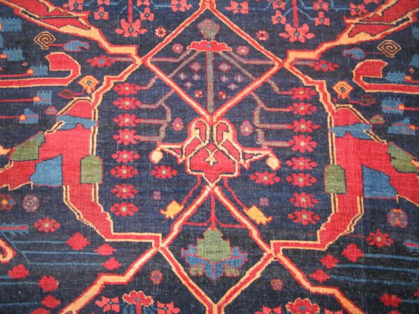 Close-up of a dark navy rug featuring geometric medallions, abstract birds, and repeating red floral motifs.