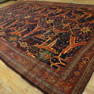 Large navy rug with a stylized red and gold pattern and multiple borders on light wooden floorboards.