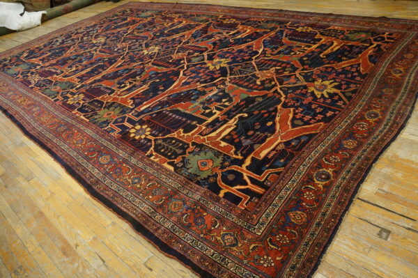 Large navy rug with a stylized red and gold pattern and multiple borders on light wooden floorboards.