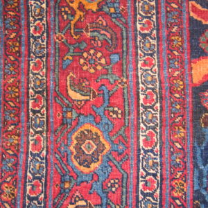 Close-up of a low-pile rug with red, navy blue, and gold traditional floral patterns over wood.
