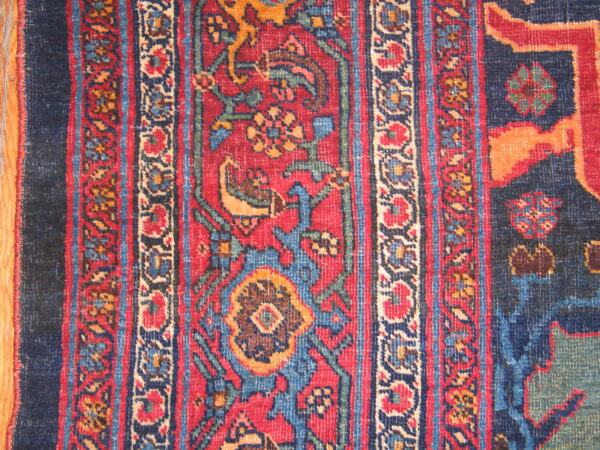 Close-up of a low-pile rug with red, navy blue, and gold traditional floral patterns over wood.