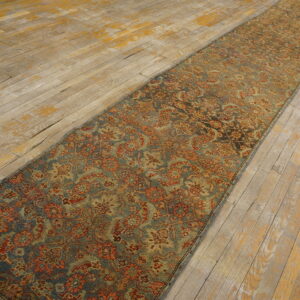 A long, narrow blue and rust traditional runner rug rests on distressed wooden floorboards.