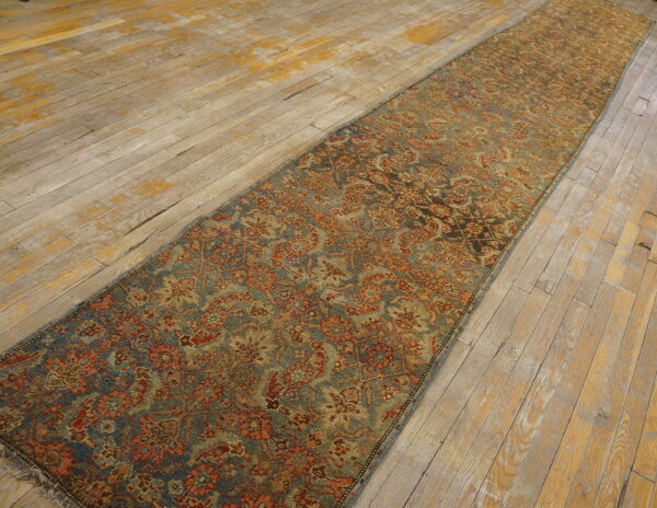 A long, narrow blue and rust traditional runner rug rests on distressed wooden floorboards.