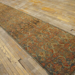 Muted blue and terracotta runner rug with a dense floral design resting on aged, wide-plank wood floor.