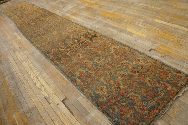 Muted blue and terracotta runner rug with a dense floral design resting on aged, wide-plank wood floor.