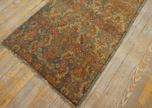 Muted blue and rust patterned rug with low pile lying on distressed light-colored wood planks.