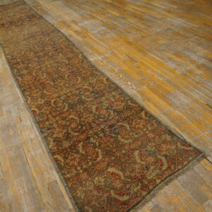 Muted red and olive patterned runner rug lying on worn hardwood flooring with distressed yellow and gray planks.
