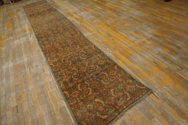 Muted red and olive patterned runner rug lying on worn hardwood flooring with distressed yellow and gray planks.
