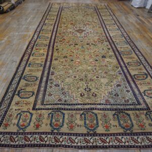 Low-pile, long rug with a pale gold field and colorful geometric patterns on distressed wood flooring.