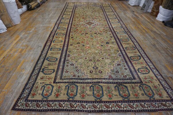 Low-pile, long rug with a pale gold field and colorful geometric patterns on distressed wood flooring.