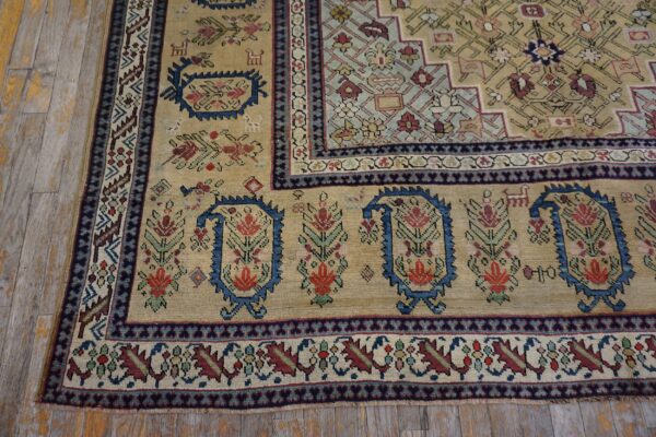 Tan rug corner with stylized floral boteh motifs in blue, red, and green on rustic wood planks.