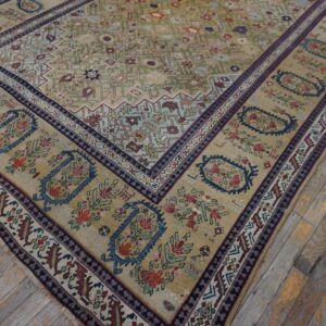Low-pile rug in tan, blue, and red traditional floral patterns rests on weathered wood planks.