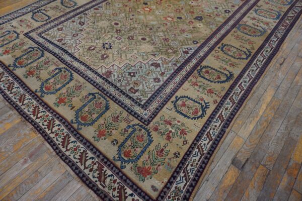 Low-pile rug in tan, blue, and red traditional floral patterns rests on weathered wood planks.