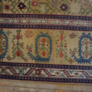 Tan rug border with wide bands of blue, red, and green stylized geometric designs on distressed wood.