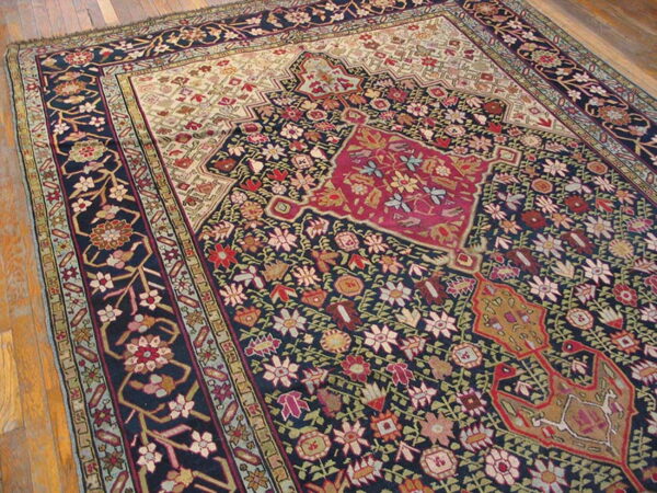Ornate navy blue rug with a dense red, cream, and multicolor floral pattern rests on wood planks.