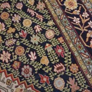 Intricate traditional rug with red, gold, and cream florals on a dark navy field, resting on gray wood.